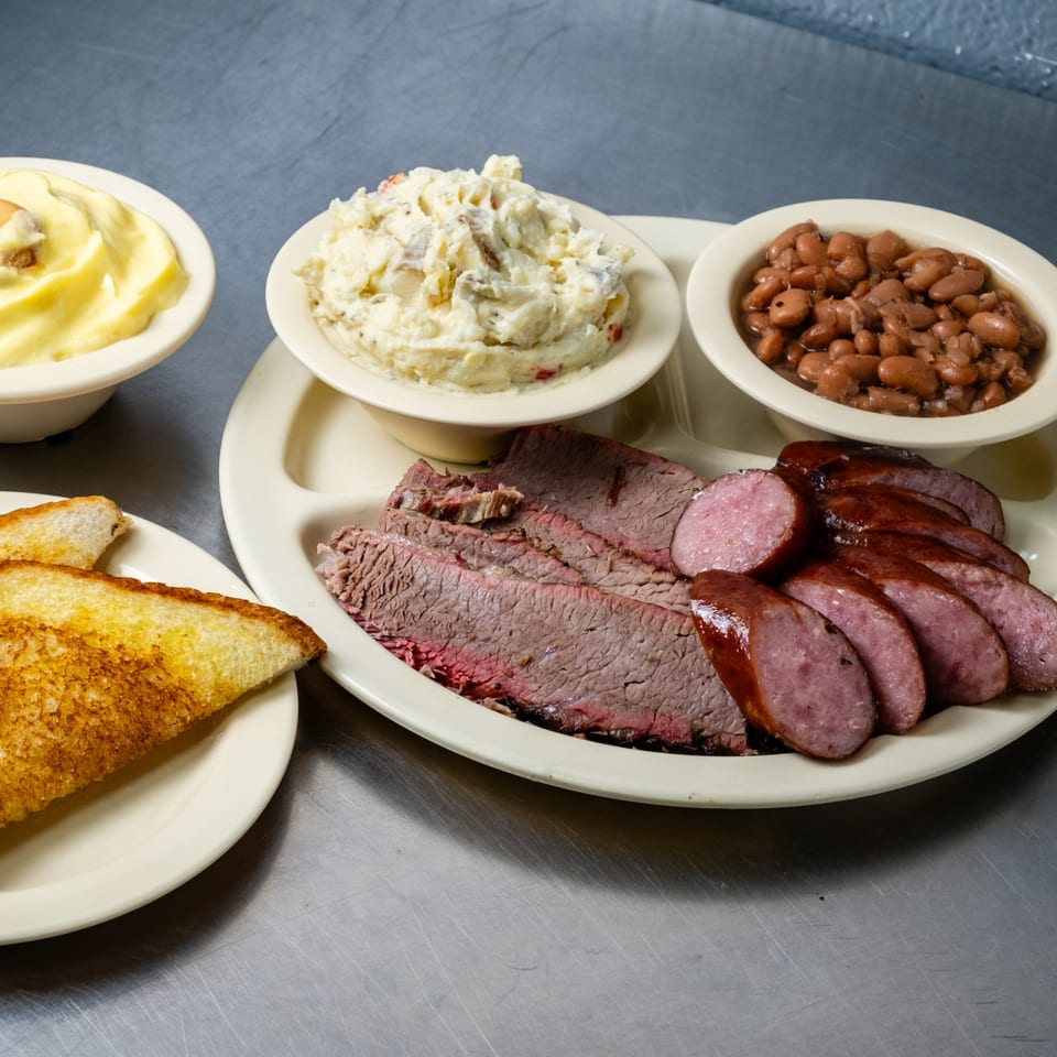 Junior's Barbeque plate with sliced brisket, sausage, baked beans, potato salad, and Texas toast.