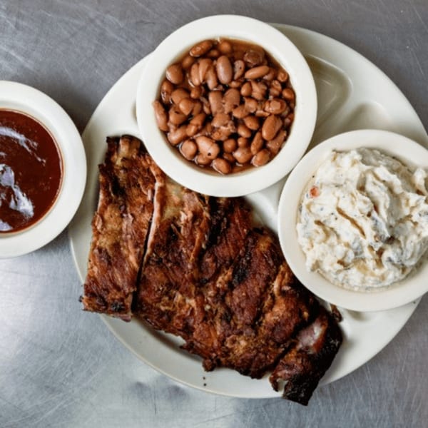 Junior's Barbeque ribs with sides of baked beans, potato salad, and a bowl of BBQ sauce.