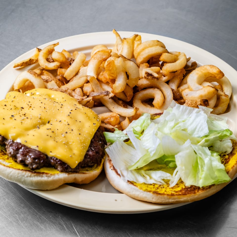 A Junior's Barbeque cheeseburger with curly fries, lettuce, and mustard on a bun.