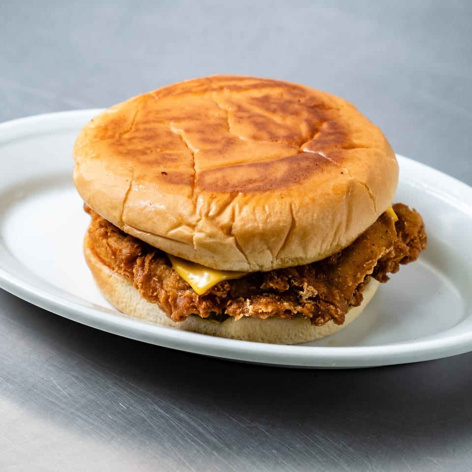 A Junior's Barbeque fried chicken sandwich with cheese on a white plate.