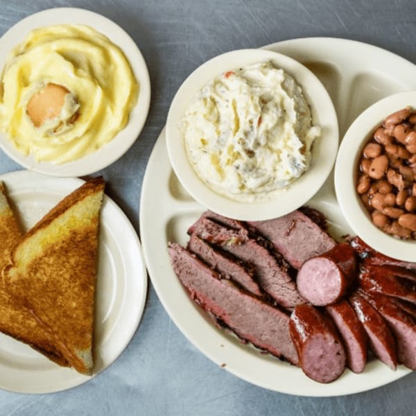 Junior's Barbeque plate with sliced brisket, sausage, baked beans, potato salad, mashed potatoes, and toast.
