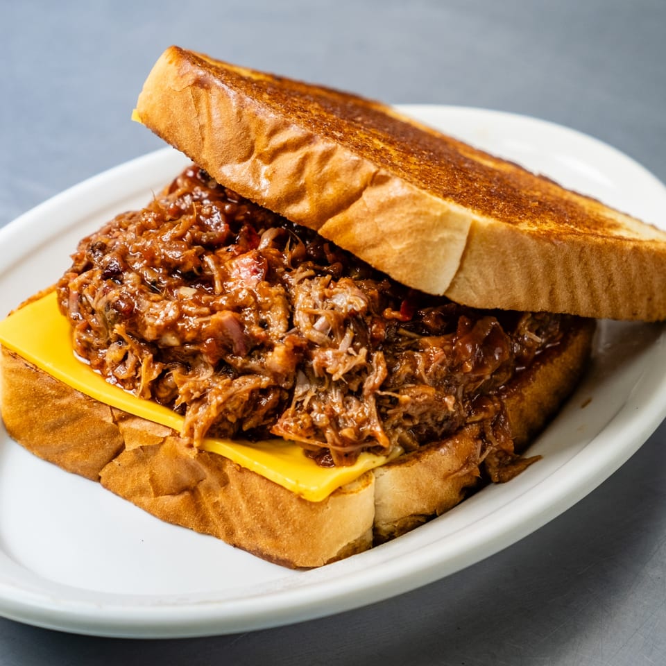 Junior's Barbeque pulled pork sandwich with melted cheese on toasted bread, served on a white plate.